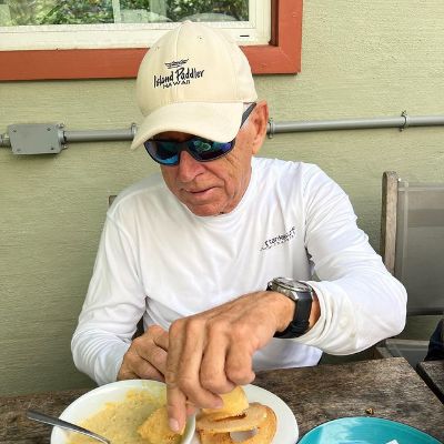 Jimmy Buffett is wearing a white shirt and a white cap as he is focused on his food.